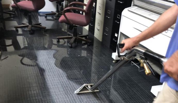 An expert using a portable extraction machine to remove water from an office carpet