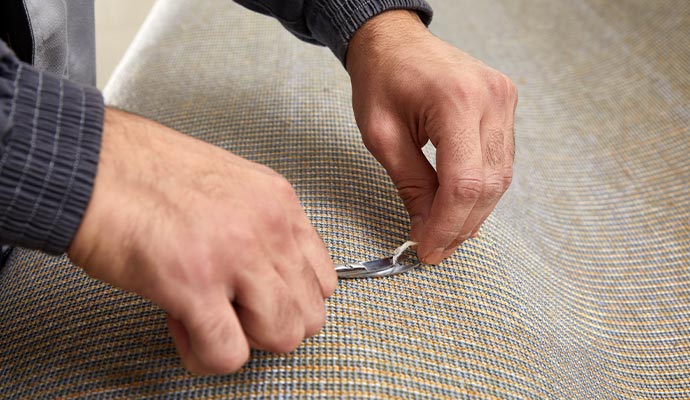 Professional worker using scissors to carefully repair a snag in a carpet.